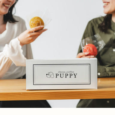 PUPPYのロゴが入った実物の白い箱を挟んで、ふたりがクッキーシューを手にするテーブル